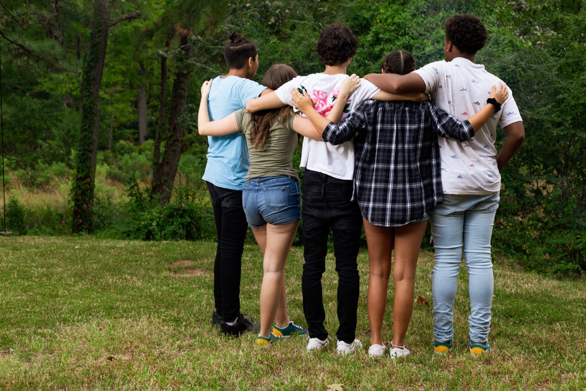 Multi-ethnic teen group in a group hug backs facing camera